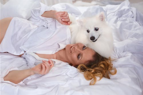 Woman Lying on a Bed with a Dog and Smiling 