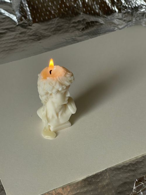 Free A melting bust-shaped candle with a bright flame on a reflective surface, adding warmth to decor. Stock Photo