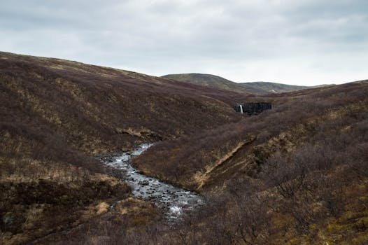 Explore the serene beauty of Iceland's rugged landscape featuring a cascading waterfall and tranquil river.