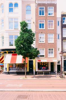 Bright Amsterdam street scene featuring traditional townhouses and storefronts in summer.