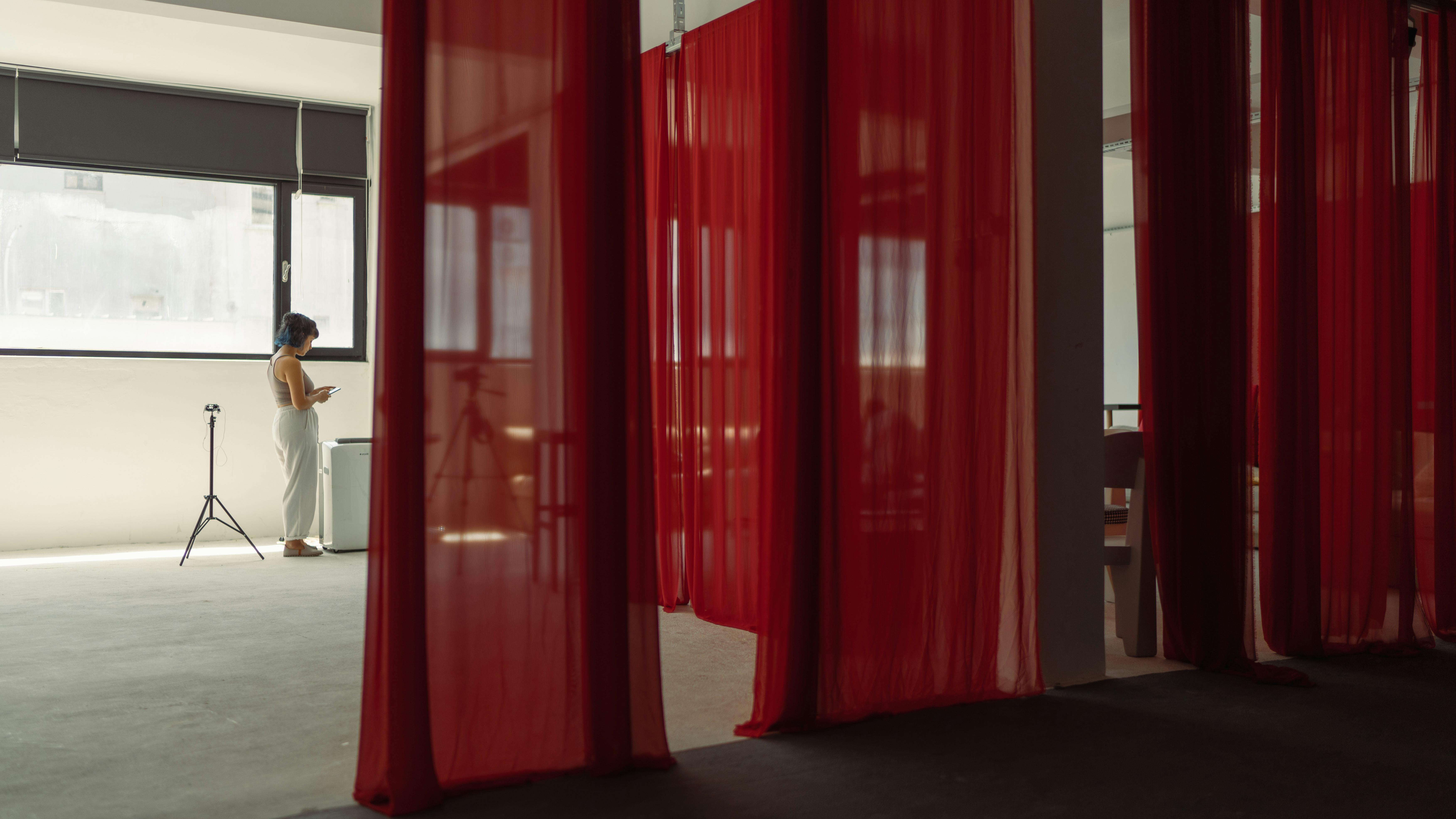 Modern studio scene with a woman, red curtains, and photography equipment.