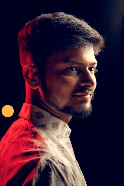 Profile portrait of a young man with a beard illuminated by red lighting in a studio.