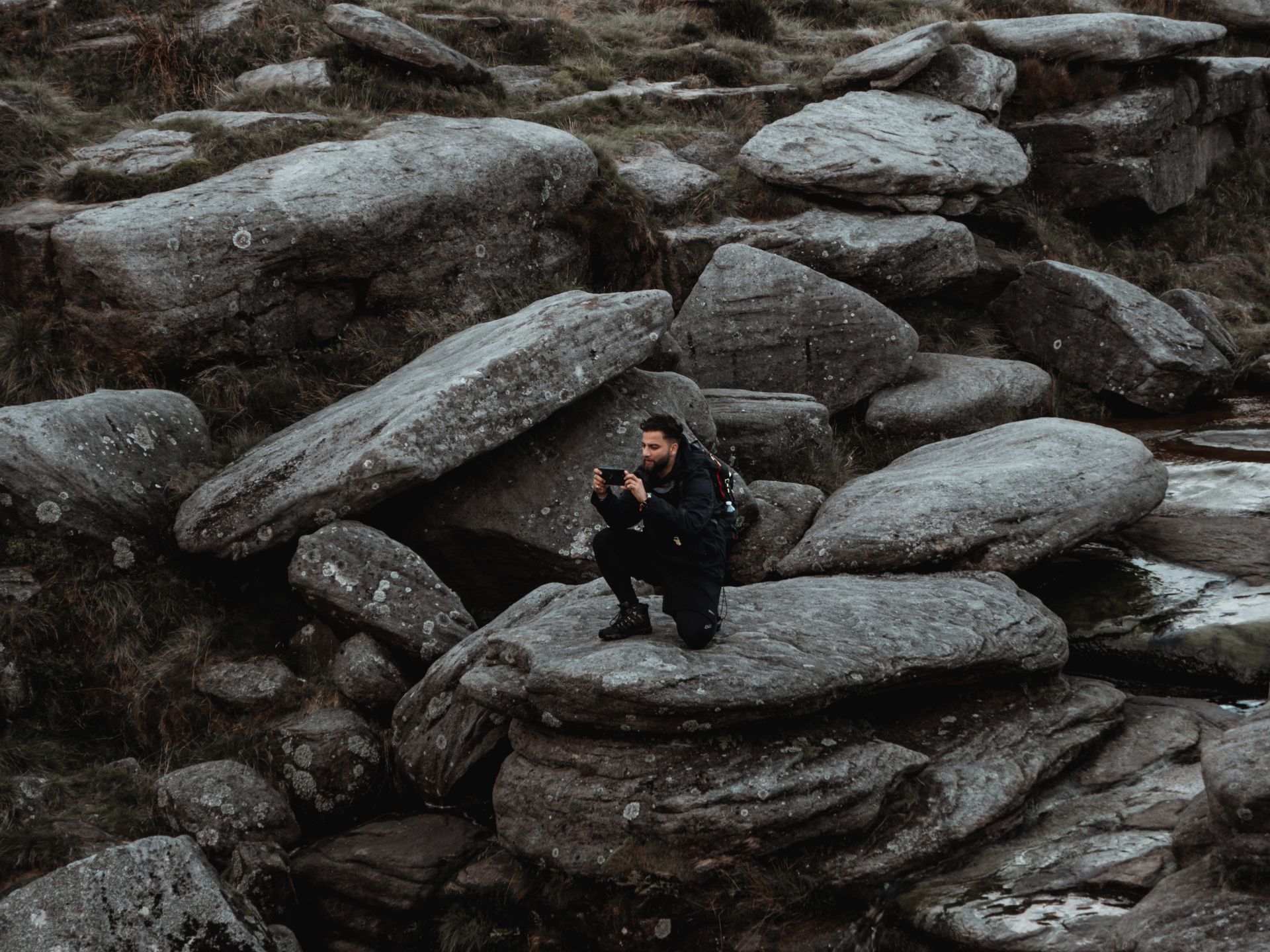 A man captures scenic rocky terrain on his smartphone while hiking in rural nature.