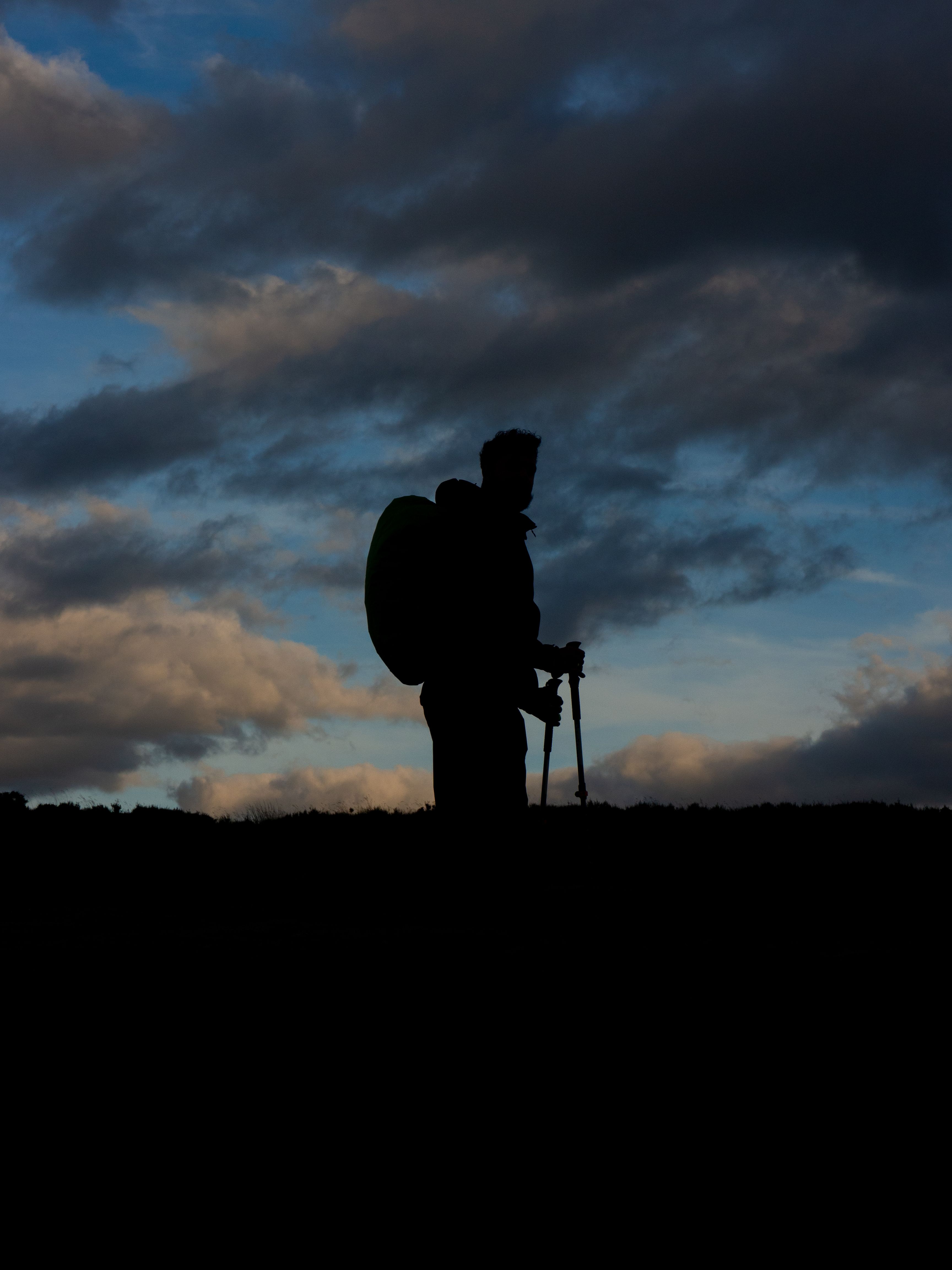 Silhouette of a person carrying a loaded backpack against a deep blue dusk sky