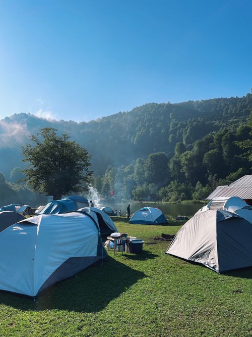 Free Peaceful campsite with tents, forest, and lake backdrop under a clear blue sky. Stock Photo