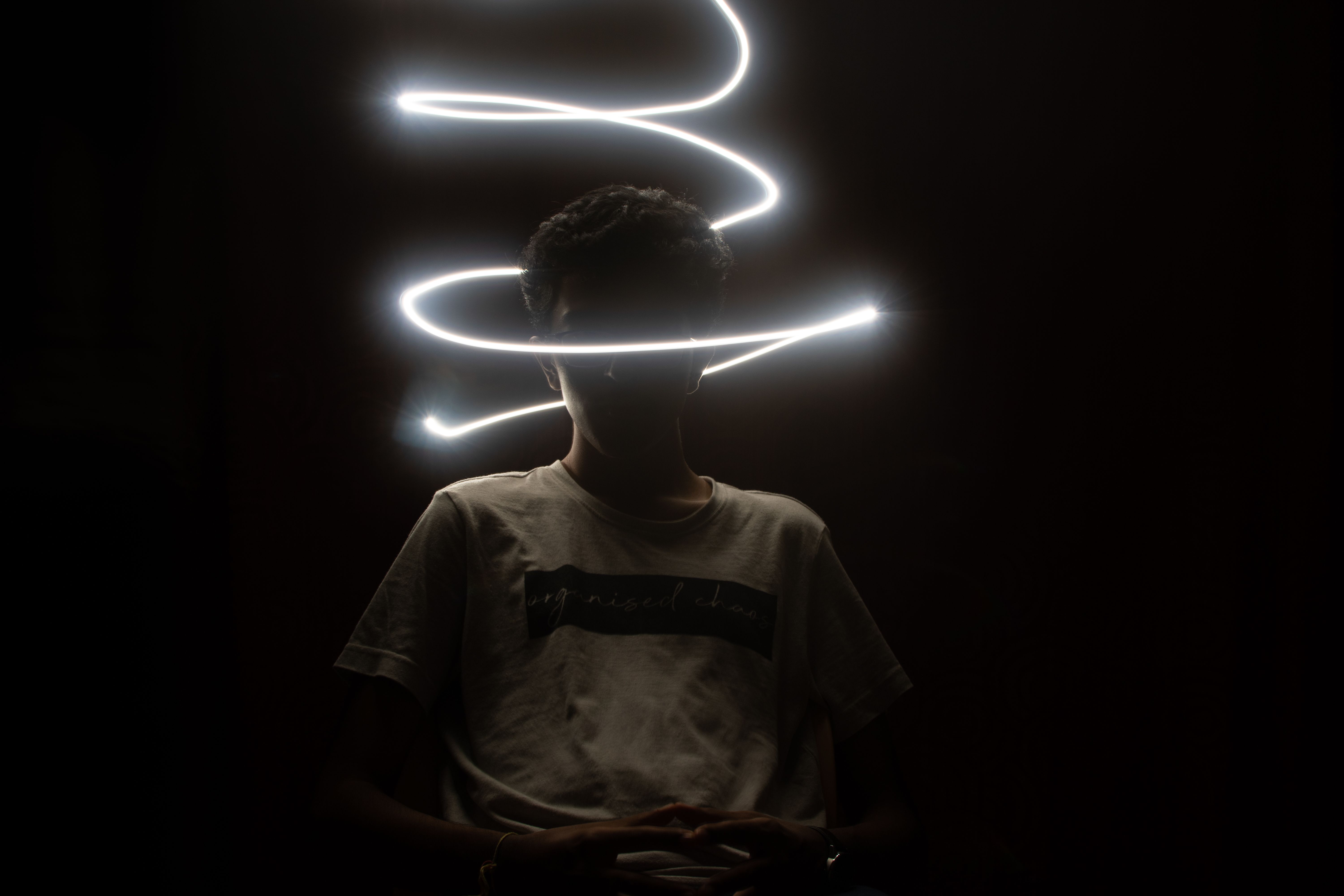 Artistic silhouette of a person encircled by swirling neon light streaks in a dark setting.