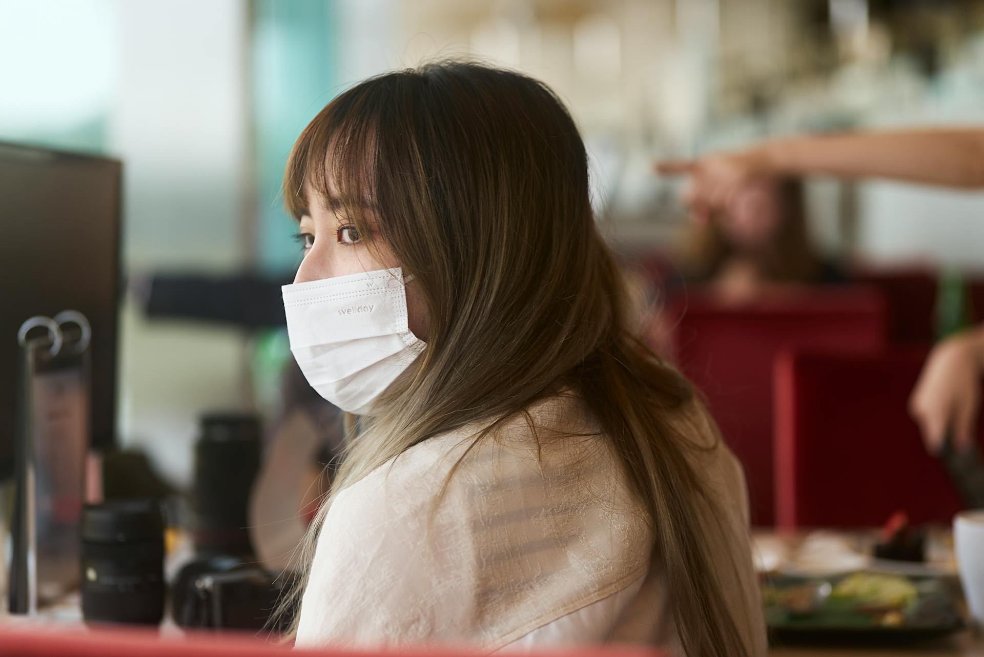 Asian woman sitting in a Singapore cafe, wearing a face mask, looking over her shoulder.