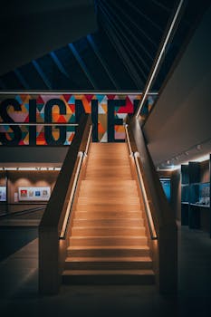 Futuristic staircase with a vibrant neon sign in a London gallery, showcasing modern architecture.