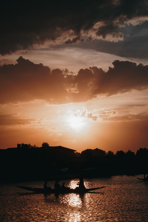 Free Silhouettes of people canoeing under a dramatic sunset sky over a tranquil river. Stock Photo