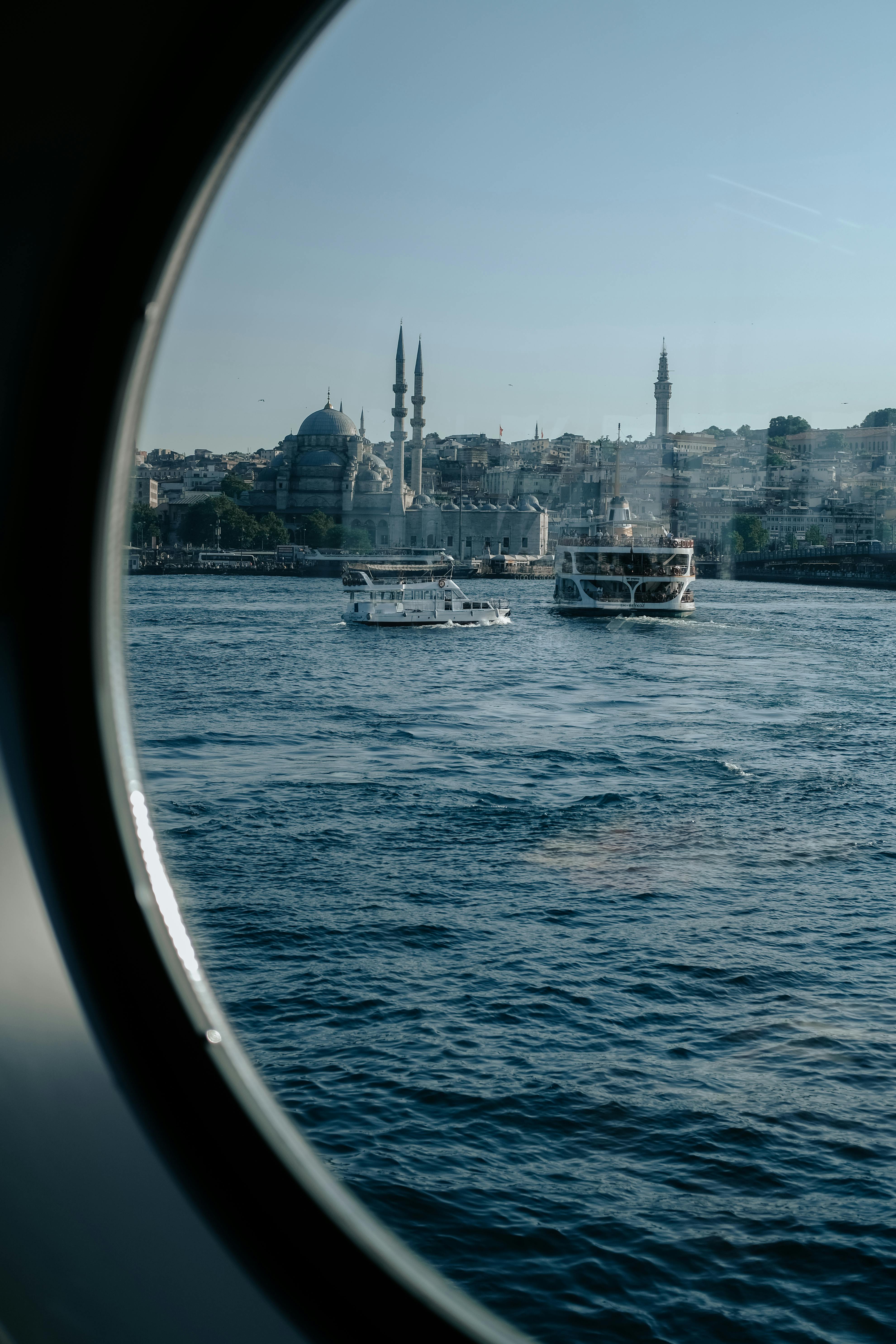 View of Istanbul's skyline with boats and mosques from a ferry window.