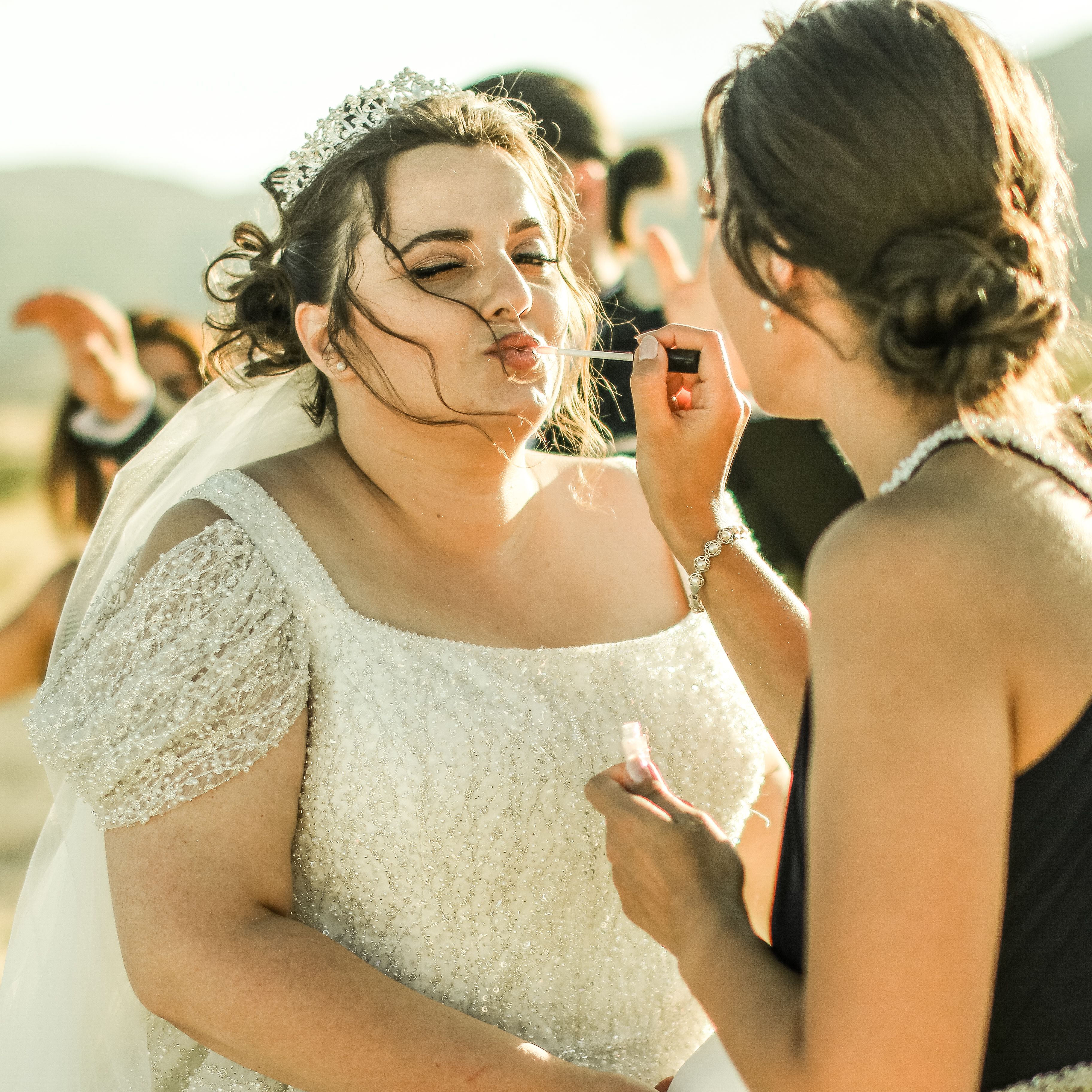 A bride gets last-minute makeup touches before her wedding ceremony outdoors.