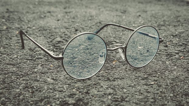 Classic round eyeglasses with a vintage design resting on textured asphalt. Ideal for retro themes.