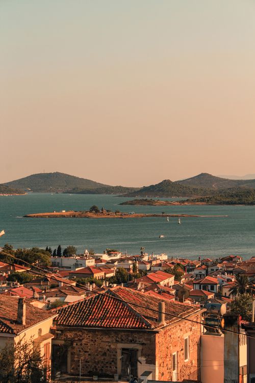 Free A scenic view of a seaside town with red rooftops overlooking an island and calm sea at sunset. Stock Photo