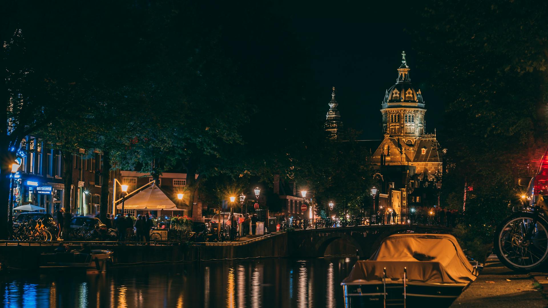 Illuminated Amsterdam canal and church at night with reflections.