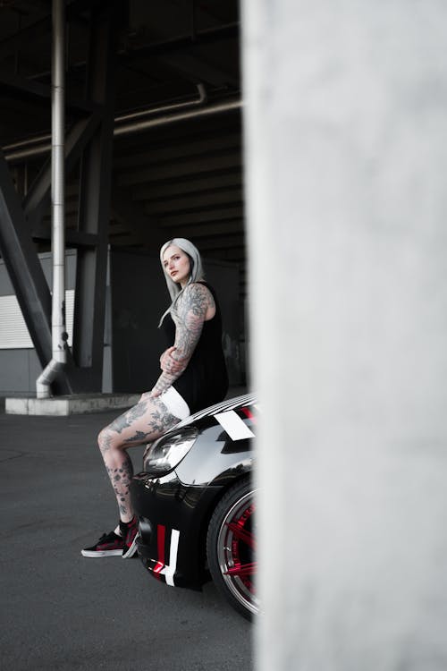 Blonde Woman with Tattoos Sitting on a Car