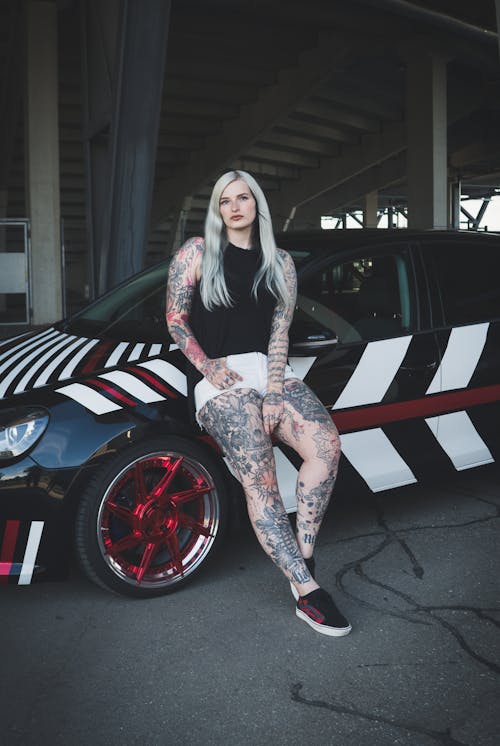 Woman with Tattoos Leaning on a Sports Car 