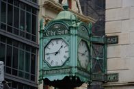 Close-up of the historic 'The Sun' clock tower in an urban setting, displaying iconic Roman numerals.