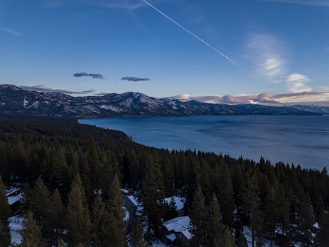 从空中俯瞰，白雪皑皑的太浩湖被松树林环绕，远处是连绵的山脉