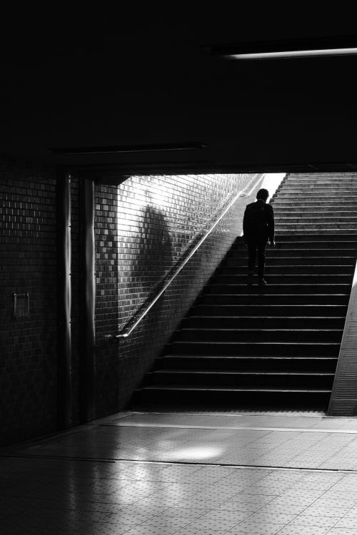 Free Black and white silhouette of a man standing at the top of stairs in an urban underground setting. Stock Photo