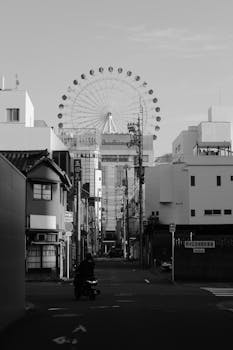 A black and white cityscape featuring a street view with a ferris wheel in the background.