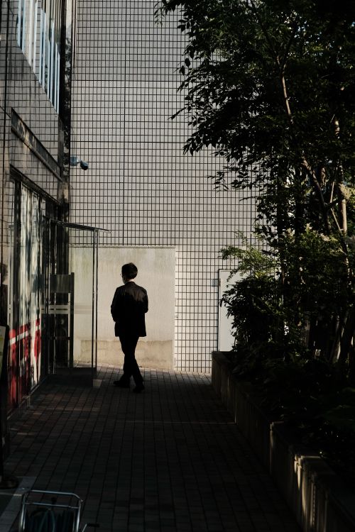 Free A man in a suit walking in an urban setting with building facades and greenery. Stock Photo