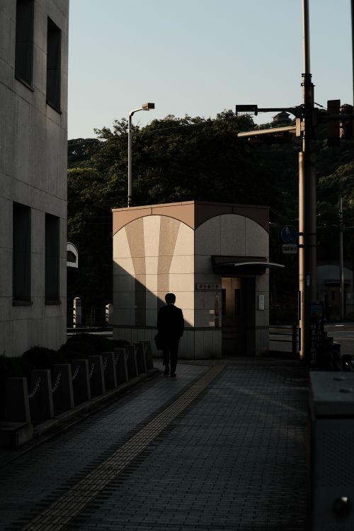 Free Silhouette of a man walking on a sidewalk in an urban area at sunset, casting long shadows. Stock Photo