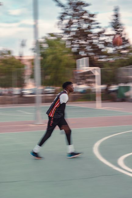 Blurred motion of a man playing basketball outdoors on a vibrant court.