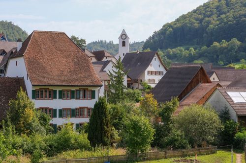 Free Idyllic view of a Swiss village with traditional houses and a church tower, surrounded by greenery. Stock Photo