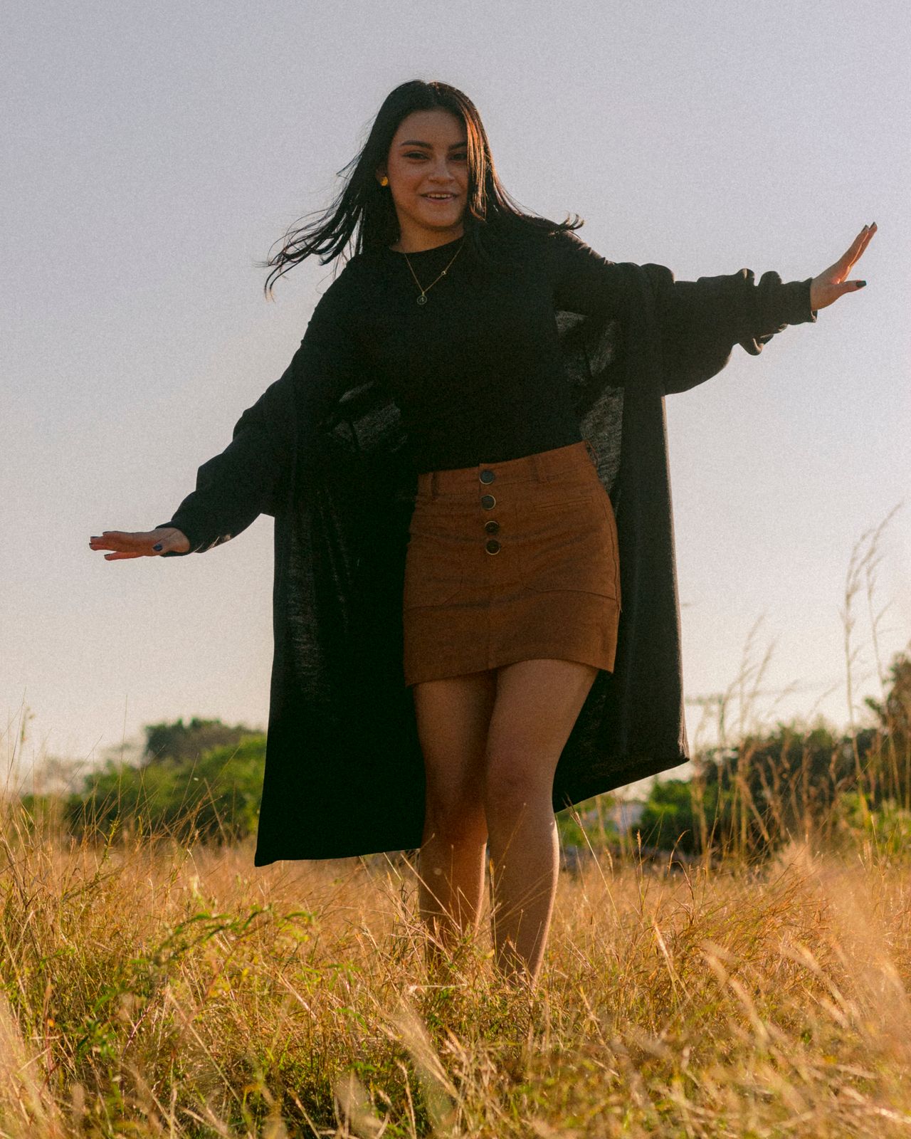Woman in a black top and brown suede mini skirt standing in tall autumn grass