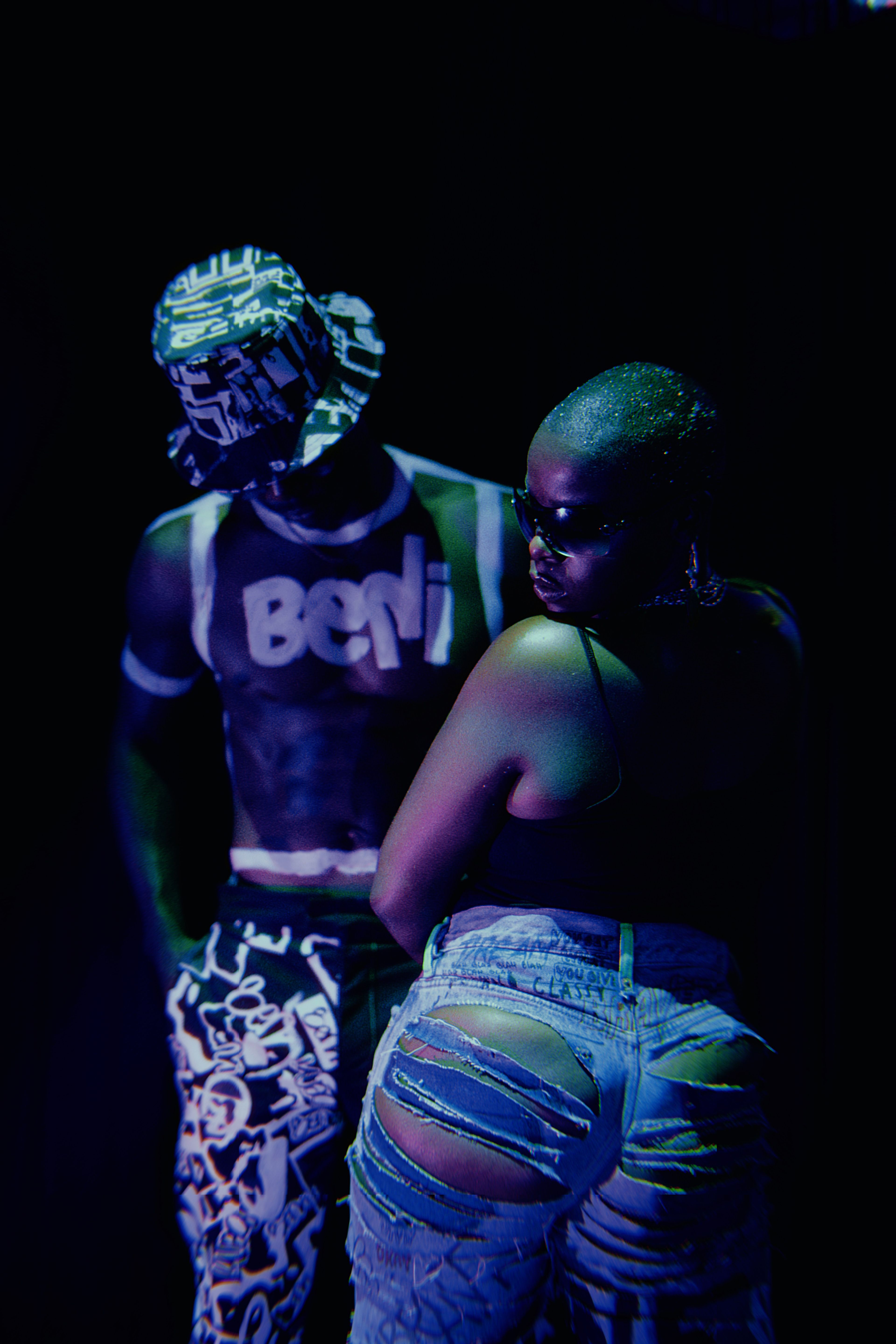 Artistic fashion studio shoot featuring a stylish couple posing against a dark background.