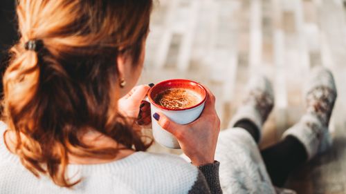Free A woman sits comfortably indoors, holding a warm cup of coffee, perfect for a cozy break. Stock Photo