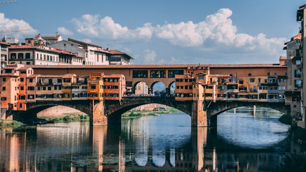 Historic Ponte Vecchio Bridge crossing over the Arno River in Florence under a blue sky.