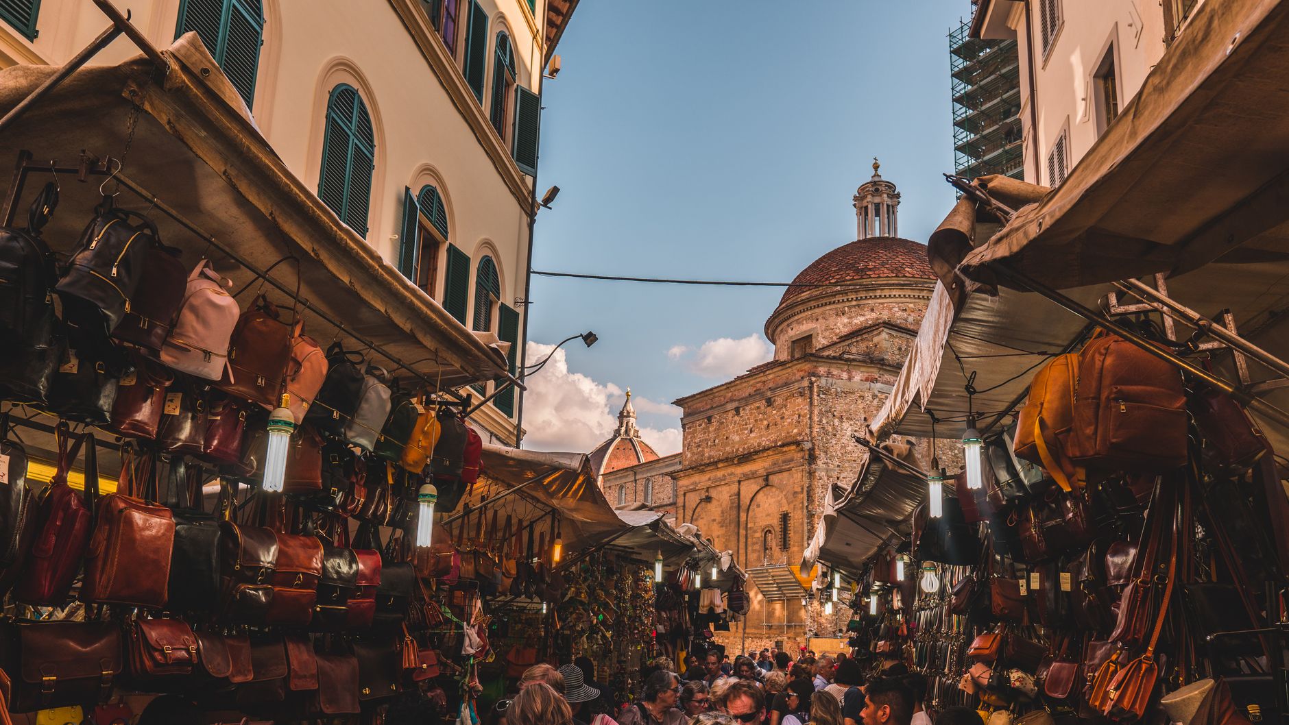 Florence leather market stalls with hanging handbags and jackets outside a historic basilica — the classic San Lorenzo shopping scene