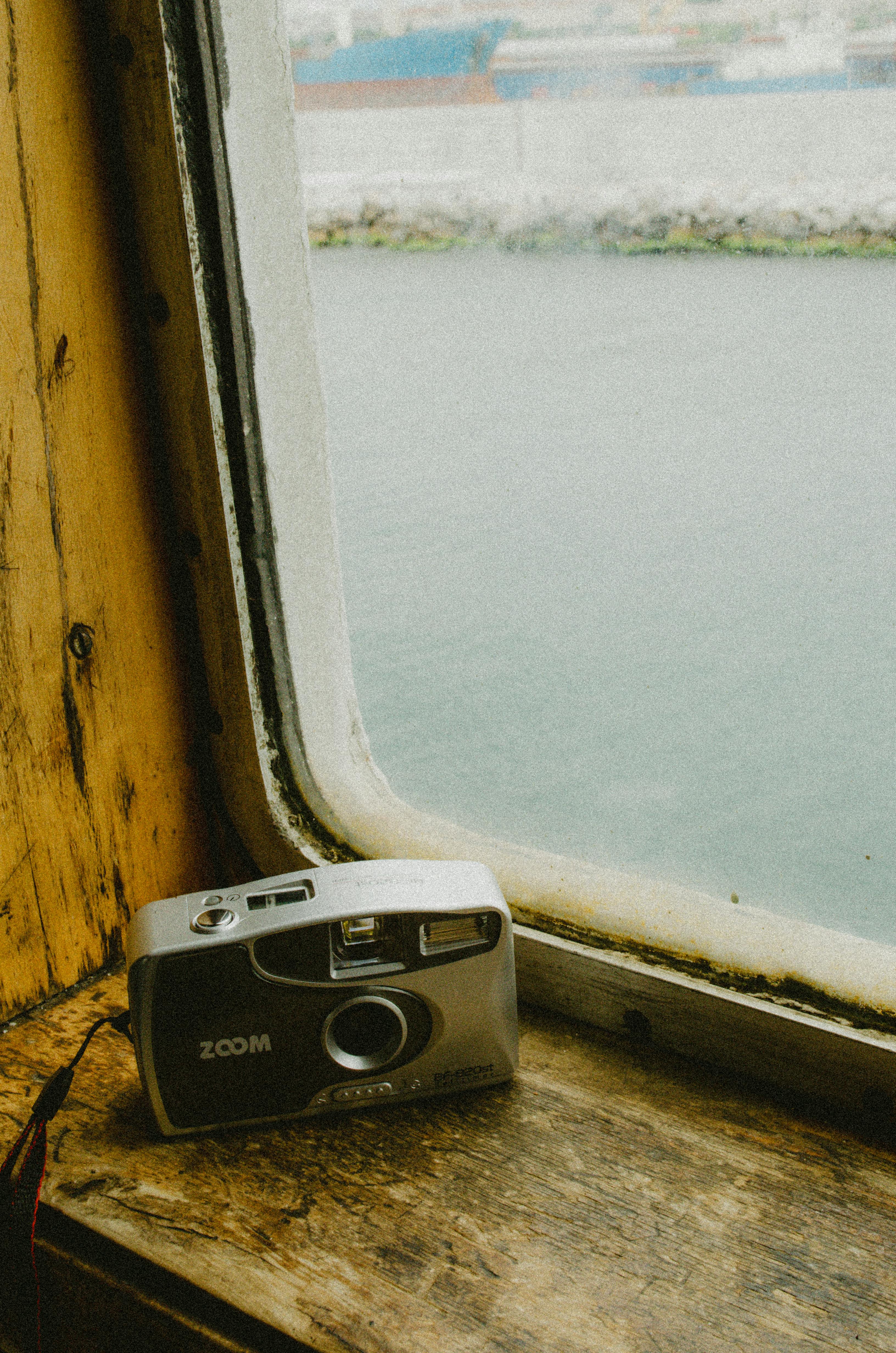 Retro film camera placed on the ledge of a ship window overlooking the sea.