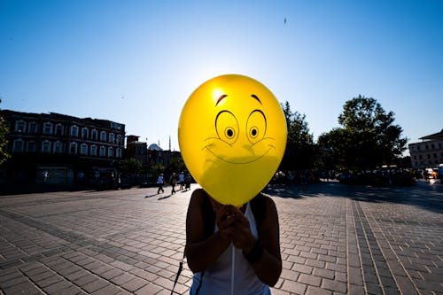 Woman Holding a Yellow Balloon with a Smiley Face in front of Her 