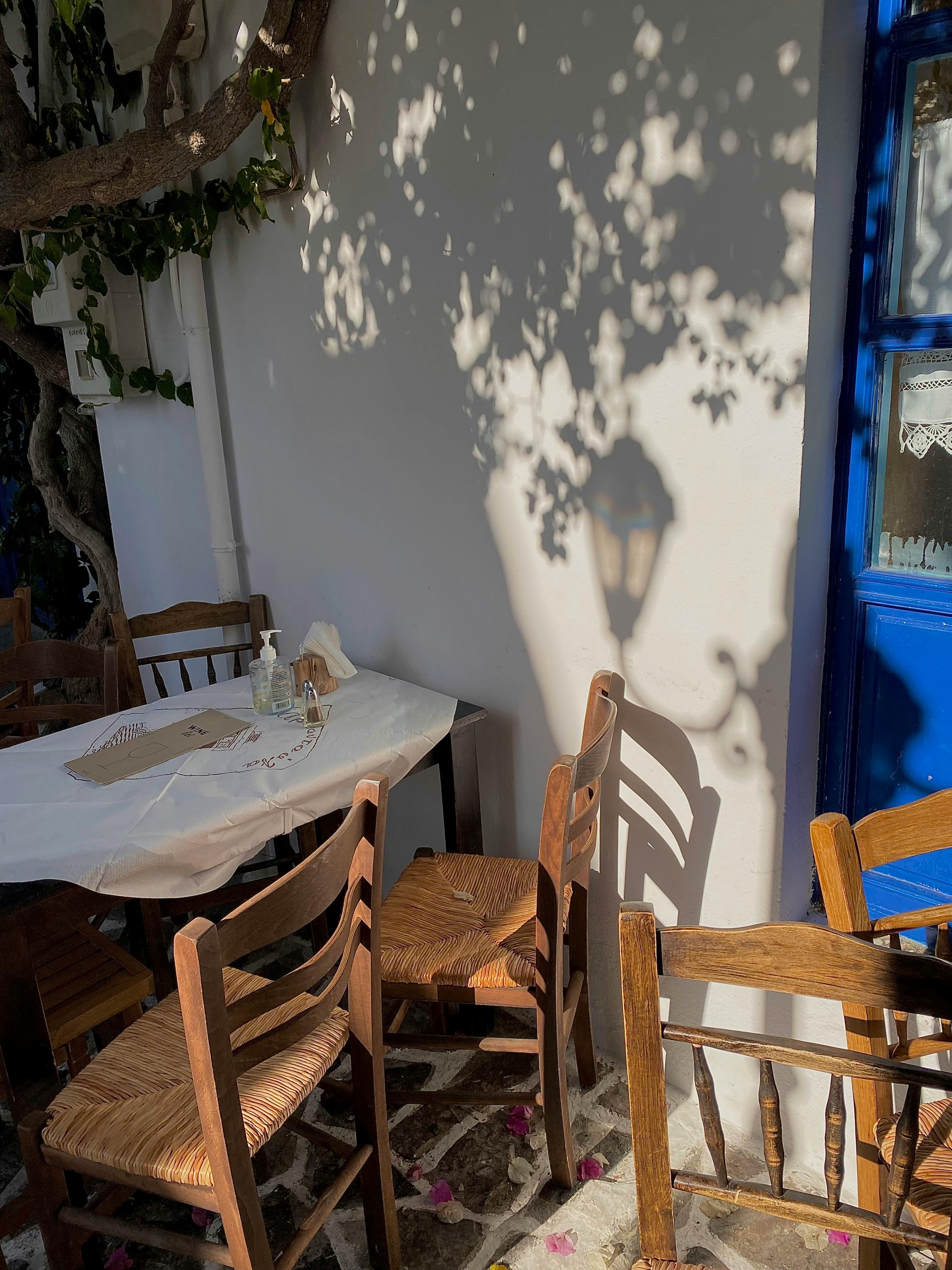 Free Cozy outdoor cafe setting with wooden chairs and a sunlit wall casting interesting shadows. Stock Photo