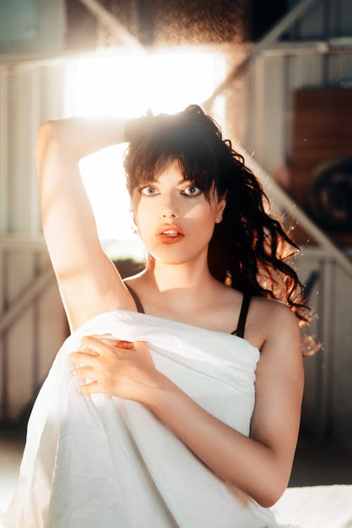 Beautiful Young Woman Posing in Bed Linen in Front of a Window