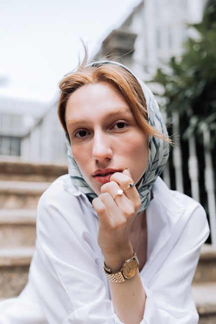Stylish portrait of a young woman in a headscarf and golden watch, sitting outdoors.
