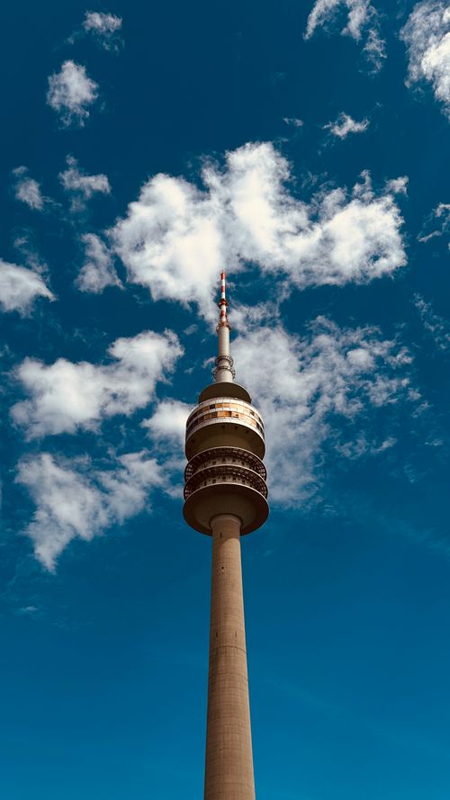 Free Low-angle view of Munich's Olympic Tower under a bright blue sky with scattered clouds. Stock Photo