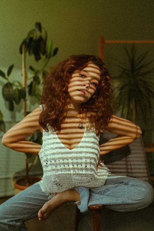 Young Woman Sitting in a Room in a Sunlight with Shadow from the Blinds 