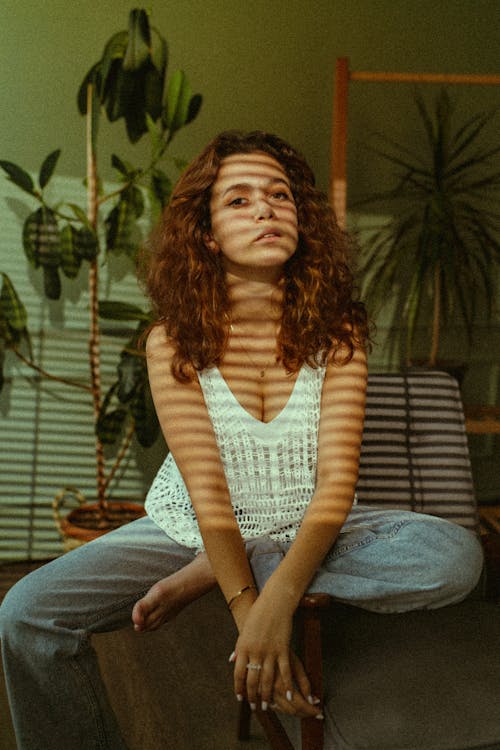 Young Woman Sitting in a Room in a Sunlight with Shadow from the Blinds 