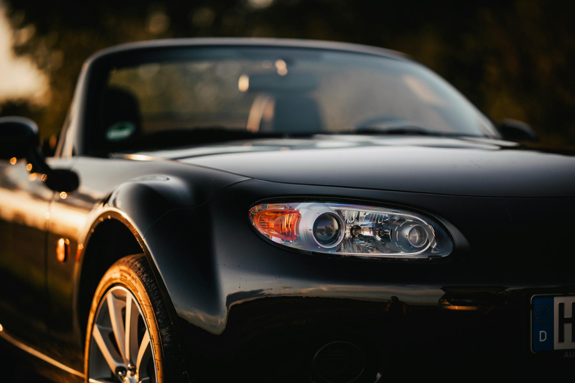 Close-up of a black Mazda MX-5 convertible reflecting sunset light, embodying modern automotive elegance.