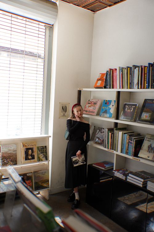 Free A young woman standing in a library, holding a book, surrounded by bookshelves. Stock Photo