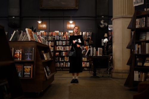 Free A young woman stands in a cozy bookstore surrounded by shelves filled with books, creating a literary ambiance. Stock Photo