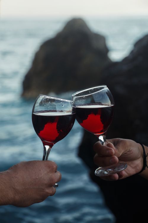 Free Two hands clinking red wine glasses with a scenic sea background in Mersin, Türkiye. Stock Photo