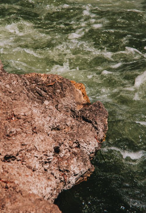 Free A close-up view of eroded rocky shore with vibrant green waves crashing against it. Stock Photo