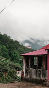 Charming rustic cabin amidst lush green forest and misty mountain landscape.