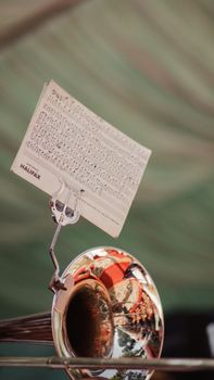A shiny trumpet with a music sheet clipped, set against an outdoor background in Muzaffarabad.