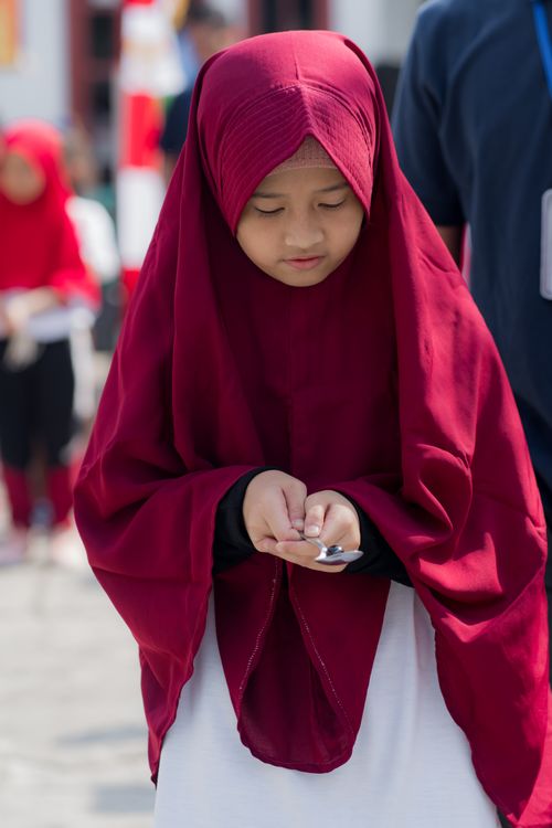 Free A young girl in traditional red attire holds a spoon during an outdoor ceremony. Stock Photo