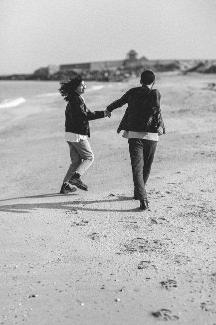 A joyful young couple holding hands running on a sandy beach, exuding happiness and romance.